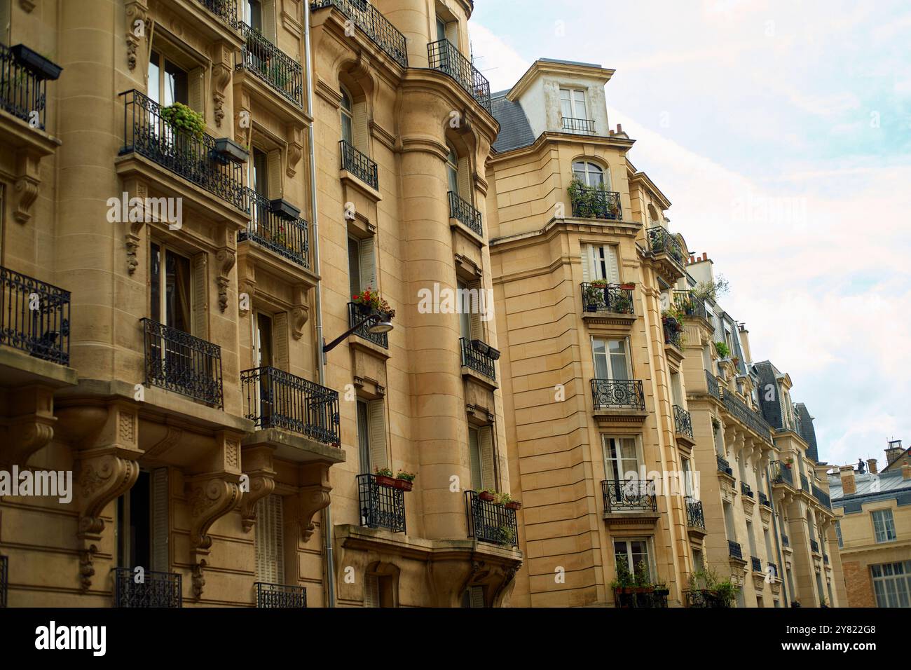 Elegante facciata di un edificio parigino con balconi e lussureggianti fioriere contro un cielo nuvoloso. Foto Stock