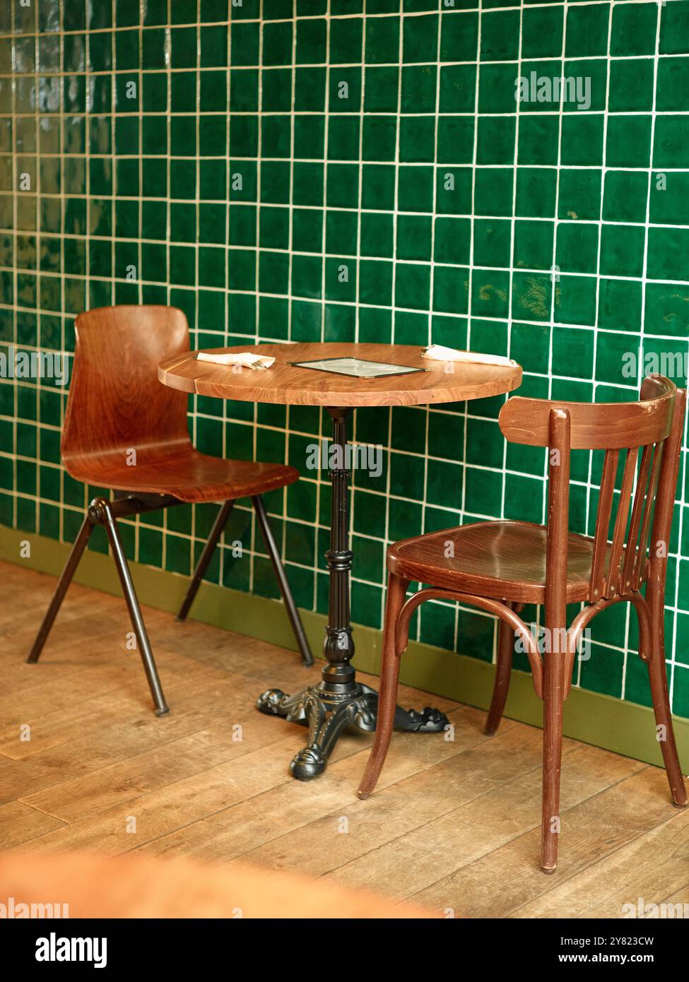 Sedie in legno vintage e tavolo rotondo su una parete piastrellata verde in un angolo accogliente. Foto Stock