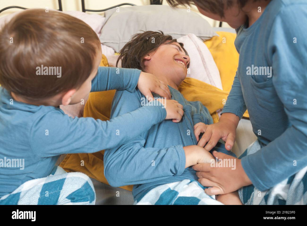 Tre bambini in pigiama giocano insieme e si fanno il solletico a letto. Scena spensierata e divertente. Foto Stock