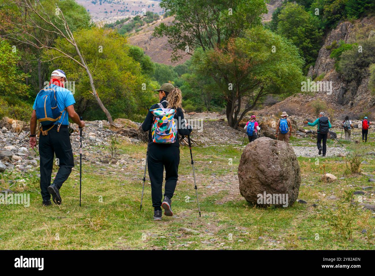 Un gruppo di escursionisti che camminano con i loro pali e zaini attraverso una valle boscosa e rocciosa. Foto Stock