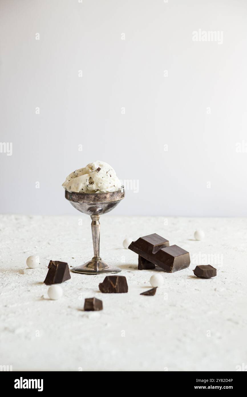 Ciotola in metallo vintage riempita con cremoso gelato alla stracciatella, decorata con pezzi di cioccolato, su uno sfondo bianco pulito per un classico bagno Foto Stock