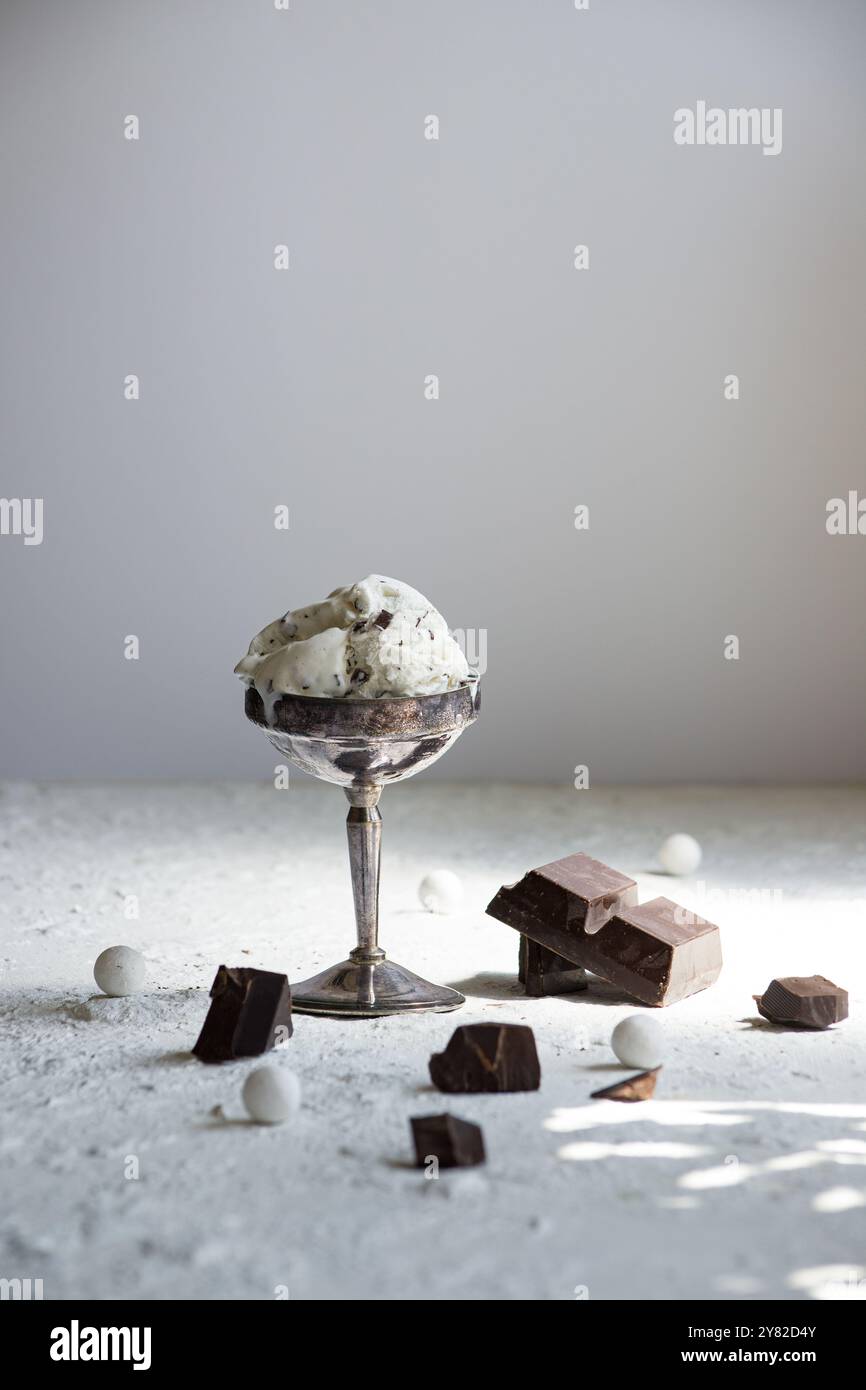 Ciotola in metallo vintage riempita con cremoso gelato alla stracciatella, decorata con pezzi di cioccolato, su uno sfondo bianco pulito per un classico bagno Foto Stock