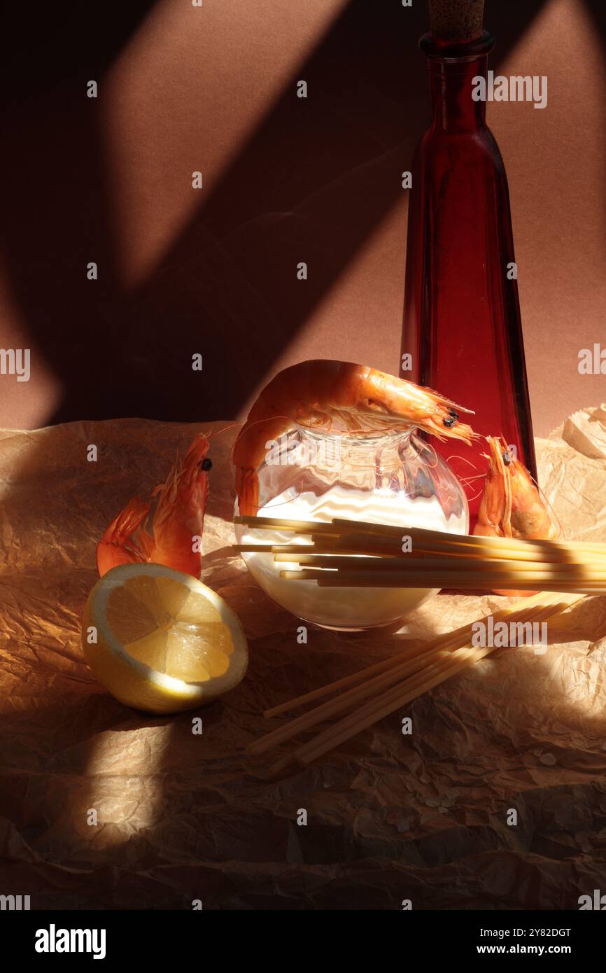 Gamberi con ingredienti per spaghetti di gamberi: Una bottiglia di olio rosso, mezzo limone e panna in una piccola bottiglia trasparente, disposti per un composto vivace e fresco Foto Stock