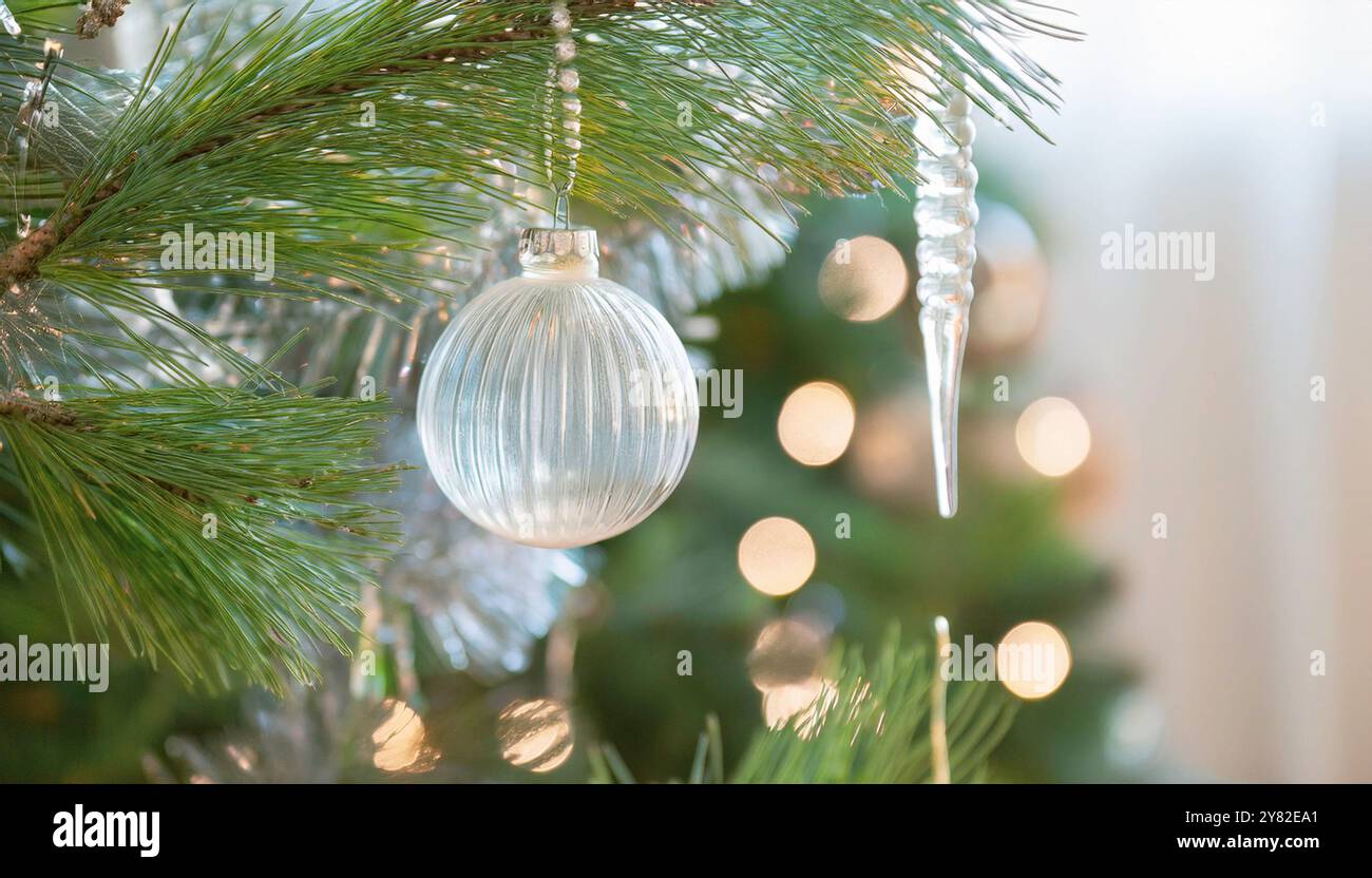 Baule natalizie in vetro appese su rami verdi di pino con luci festive, splendenti ornamenti natalizi con sfondo bokeh, elegante minimalista Foto Stock