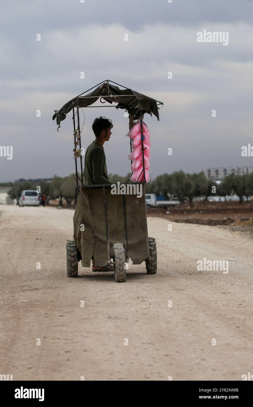Aleppo, Siria. 10 novembre 2021. Un venditore ambulante che vende filo interdentale di caramelle circondato da bambini nel campo di sfollamento di al-Zaytoun situato alla periferia della città ribelle di Azaz, nella campagna settentrionale di Aleppo. Le tende sono state allestite negli oliveti lungo il confine turco, con i residenti dell'insediamento informale e i loro figli che lottano per infrastrutture e opportunità minime oltre alla mancanza di spazio Foto Stock Aleppo, Siria. 10 novembre 2021. Un venditore ambulante che vende filo interdentale di caramelle circondato da bambini nel campo di sfollamento di al-Zaytoun situato alla periferia della città ribelle di Azaz, nella campagna settentrionale di Aleppo. Le tende sono state allestite negli oliveti lungo il confine turco, con i residenti dell'insediamento informale e i loro figli che lottano per infrastrutture e opportunità minime oltre alla mancanza di spazio Foto Stock