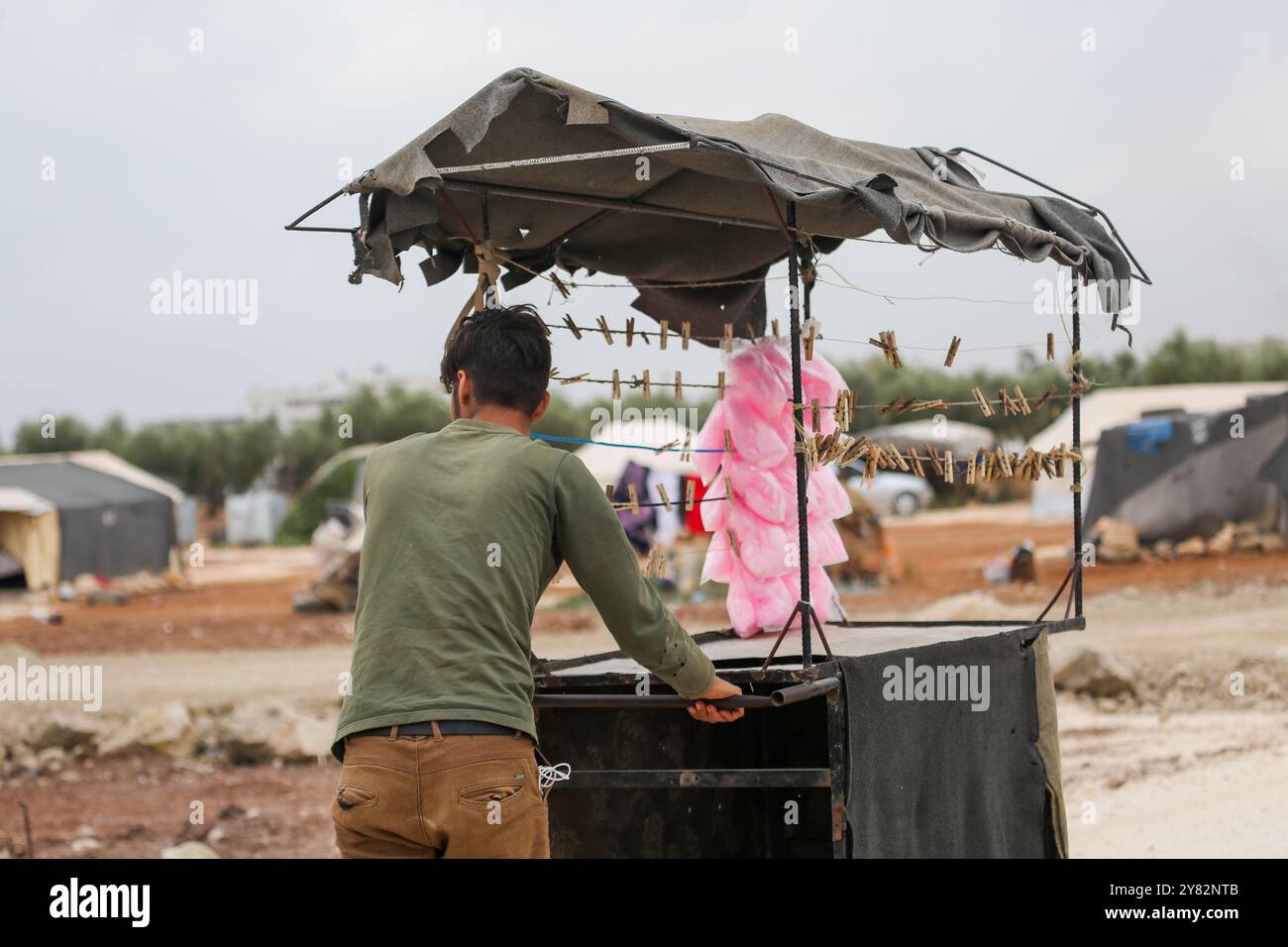 Aleppo, Siria. 10 novembre 2021. Un venditore ambulante che vende filo interdentale di caramelle circondato da bambini nel campo di sfollamento di al-Zaytoun situato alla periferia della città ribelle di Azaz, nella campagna settentrionale di Aleppo. Le tende sono state allestite negli oliveti lungo il confine turco, con i residenti dell'insediamento informale e i loro figli che lottano per infrastrutture e opportunità minime oltre alla mancanza di spazio Foto Stock Aleppo, Siria. 10 novembre 2021. Un venditore ambulante che vende filo interdentale di caramelle circondato da bambini nel campo di sfollamento di al-Zaytoun situato alla periferia della città ribelle di Azaz, nella campagna settentrionale di Aleppo. Le tende sono state allestite negli oliveti lungo il confine turco, con i residenti dell'insediamento informale e i loro figli che lottano per infrastrutture e opportunità minime oltre alla mancanza di spazio Foto Stock