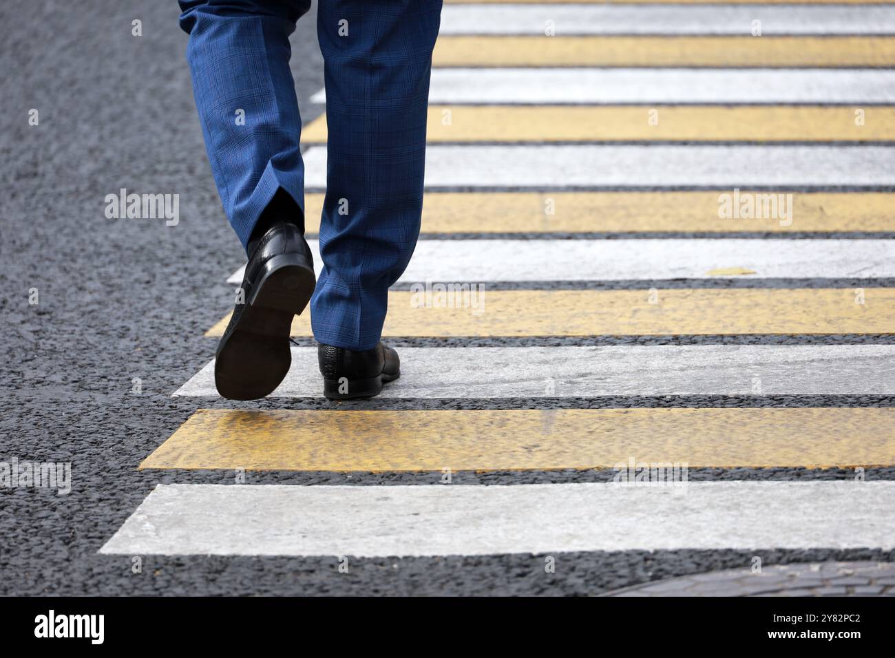 Uomo che indossa una tuta da lavoro che attraversa la strada a un incrocio. Gambe maschili sull'attraversamento pedonale Foto Stock