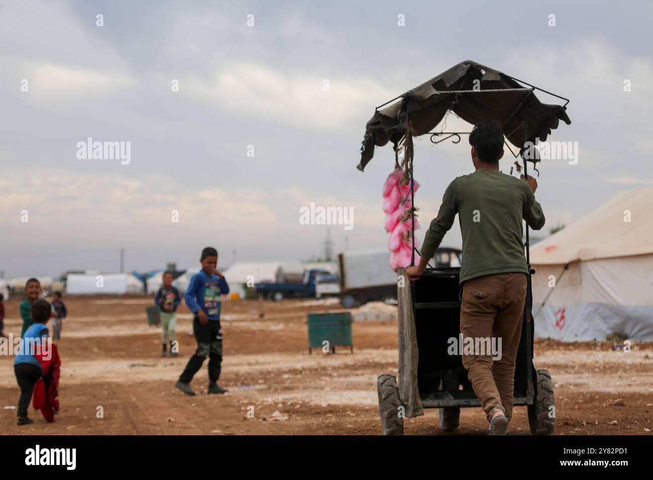 Aleppo, Siria. 10 novembre 2021. Un venditore ambulante che vende filo interdentale di caramelle circondato da bambini nel campo di sfollamento di al-Zaytoun situato alla periferia della città ribelle di Azaz, nella campagna settentrionale di Aleppo. Le tende sono state allestite negli oliveti lungo il confine turco, con i residenti dell'insediamento informale e i loro figli che lottano per infrastrutture e opportunità minime oltre alla mancanza di spazio Foto Stock Aleppo, Siria. 10 novembre 2021. Un venditore ambulante che vende filo interdentale di caramelle circondato da bambini nel campo di sfollamento di al-Zaytoun situato alla periferia della città ribelle di Azaz, nella campagna settentrionale di Aleppo. Le tende sono state allestite negli oliveti lungo il confine turco, con i residenti dell'insediamento informale e i loro figli che lottano per infrastrutture e opportunità minime oltre alla mancanza di spazio Foto Stock