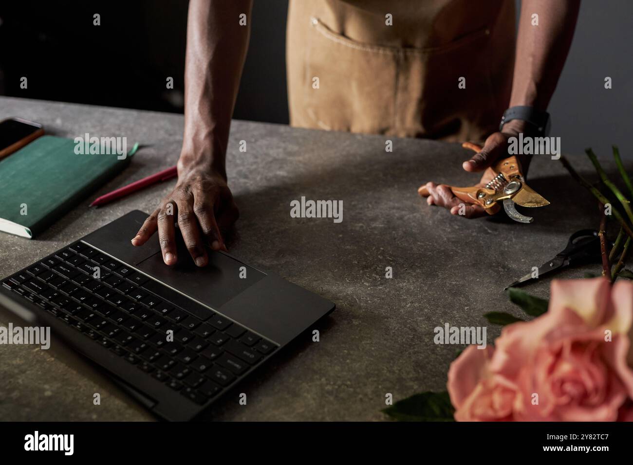 Primo piano minimale dell'irriconoscibile uomo nero come artigiano o fioraio che utilizza un computer portatile con spazio per copie dai colori scuri Foto Stock