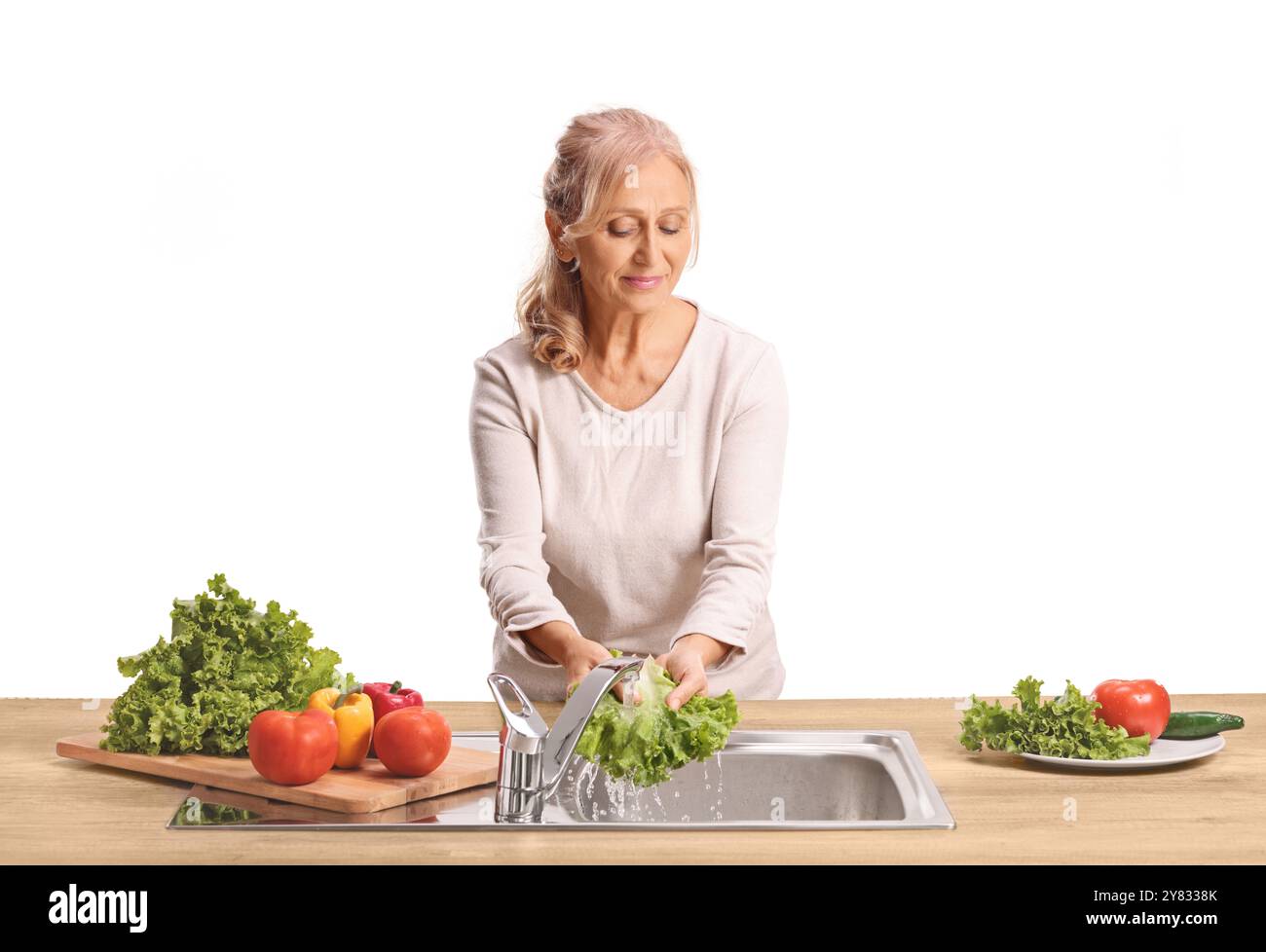 Donna che lava le verdure in un lavandino della cucina e sorride isolata su sfondo bianco Foto Stock