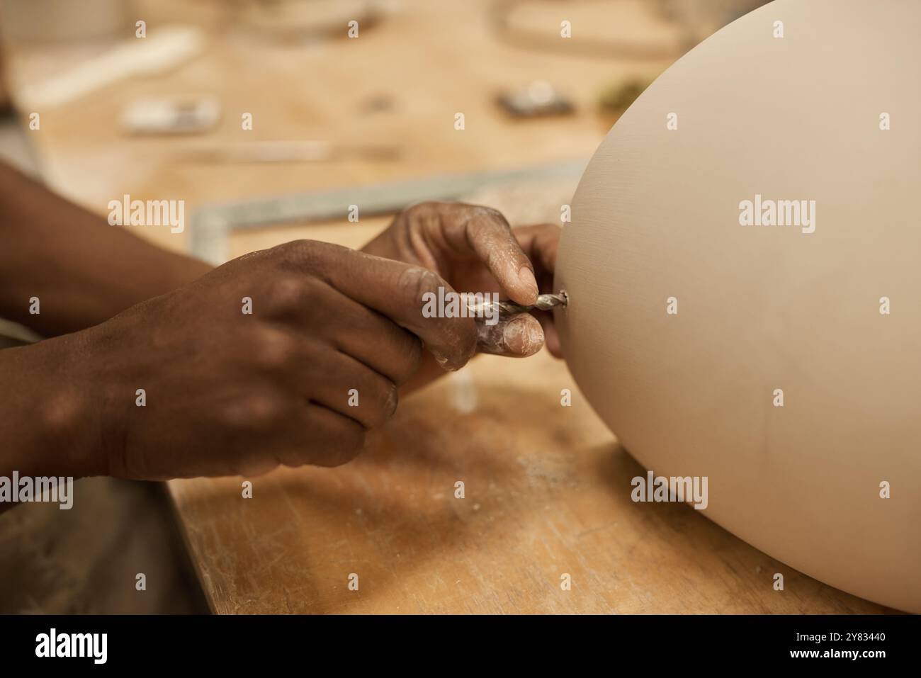 Primo piano di un ceramista africano che utilizza una punta per realizzare un foro in una pentola di argilla, su un banco in un'officina di produzione di ceramiche Foto Stock