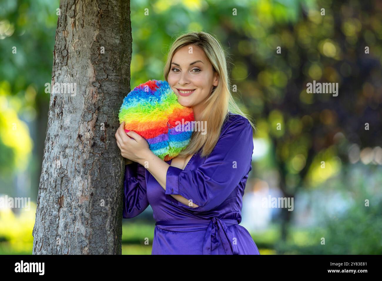 Bella donna con capelli lunghi e abito viola si sta godendo nel gioco nel parco pubblico con palla colorata. Foto Stock