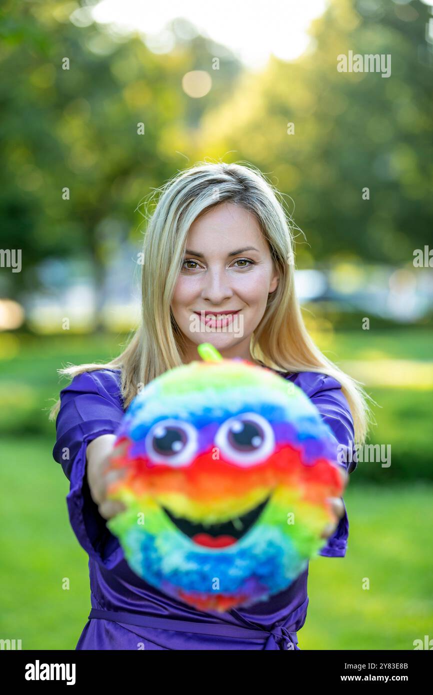 Bella donna con capelli lunghi e abito viola si sta godendo nel gioco nel parco pubblico con palla colorata. Foto Stock