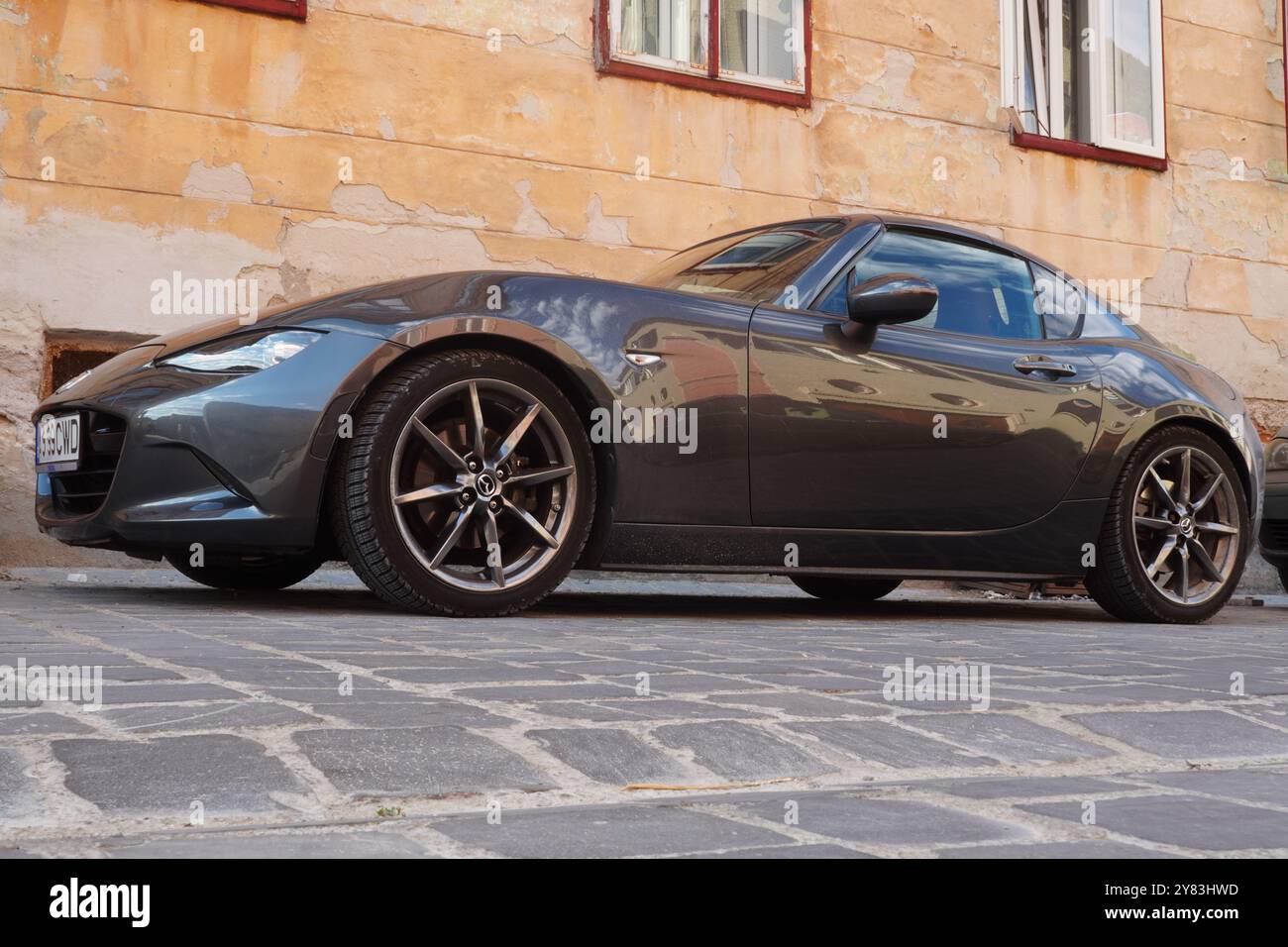 Brasov, Romania - 18 agosto 2024: Mazda MX-5 auto nera parcheggiata in una strada acciottolata in origine alla vecchia casa nel centro storico della città Foto Stock