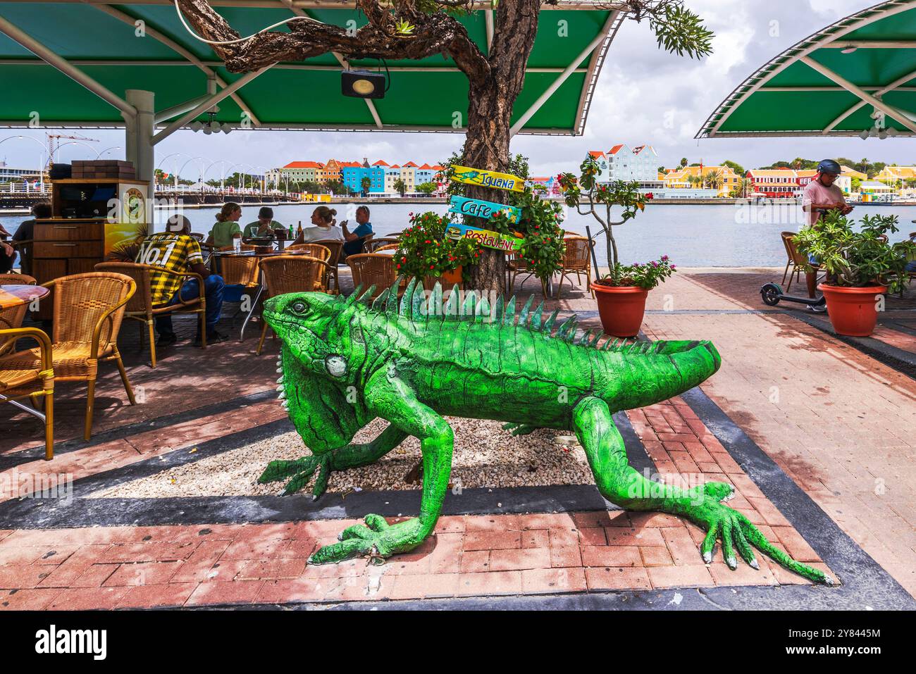 Caffè all'aperto con grande scultura di iguana di fronte al lungomare di Curacao, con edifici colorati sullo sfondo. Curacao. Willemstad. Foto Stock