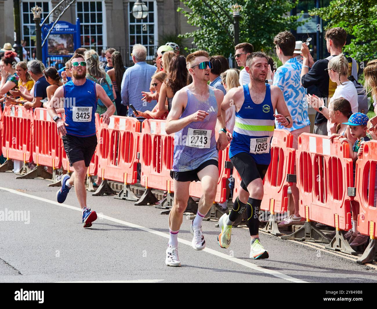 Tre runner maschili in forma che indossano una spinta sul tratto finale di una mezza maratona sostenuta da folle di tifosi. Foto Stock