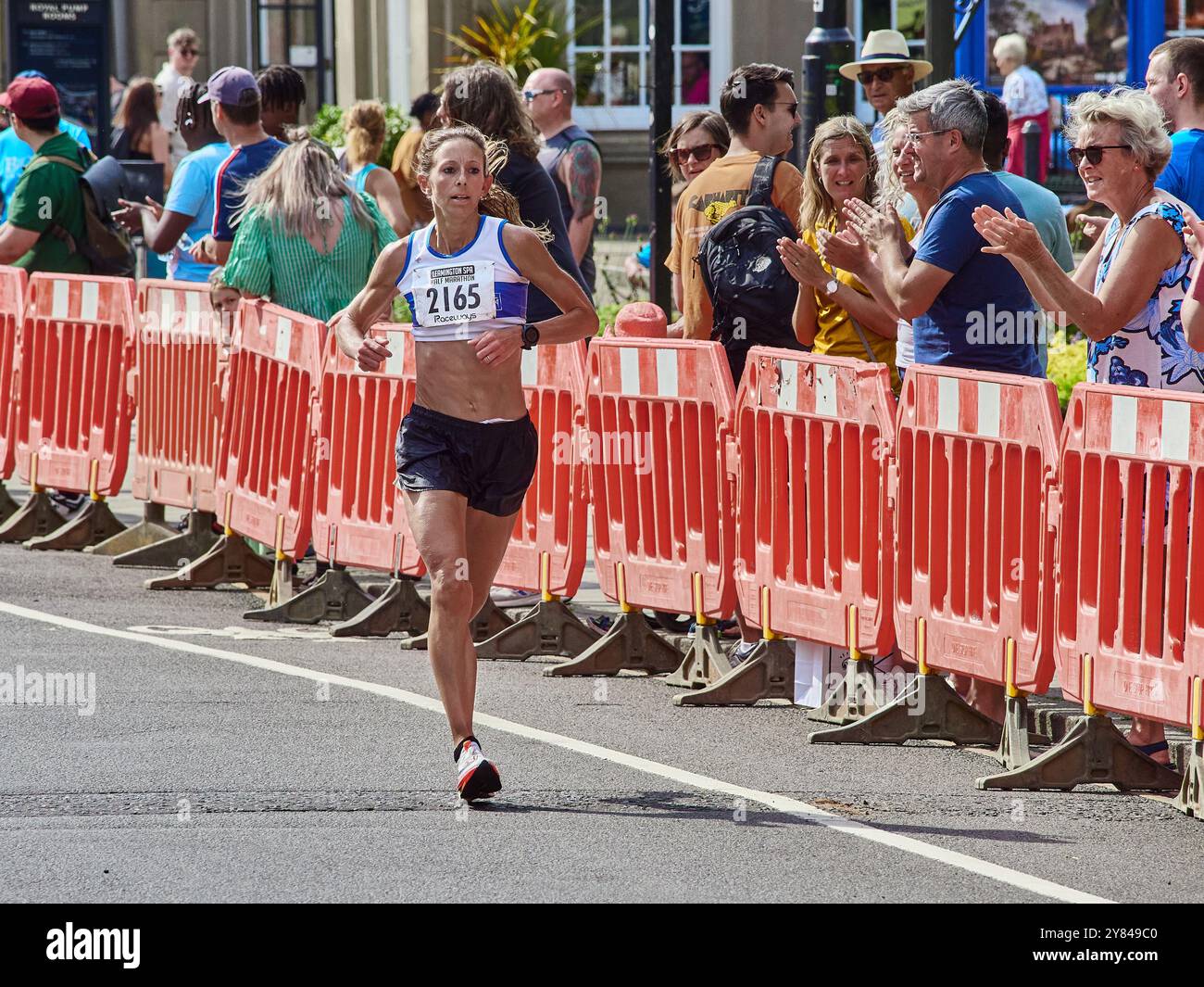 Calzate una runner femminile che indossa un colpo sul tratto finale di una mezza maratona sostenuta da una folla di tifo. Foto Stock