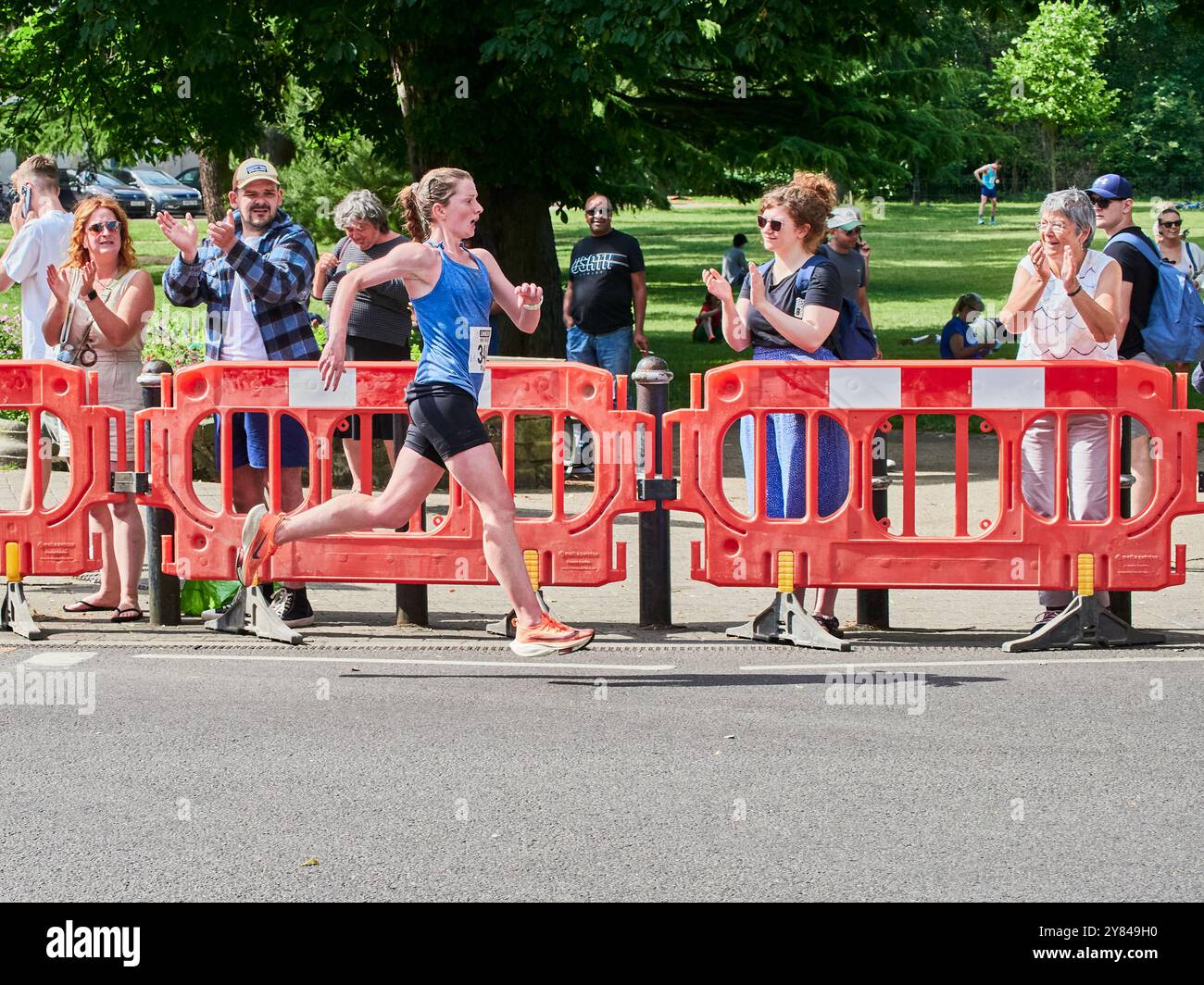 Calzate una runner femminile che indossa un colpo sul tratto finale di una mezza maratona sostenuta da una folla di tifo. Foto Stock