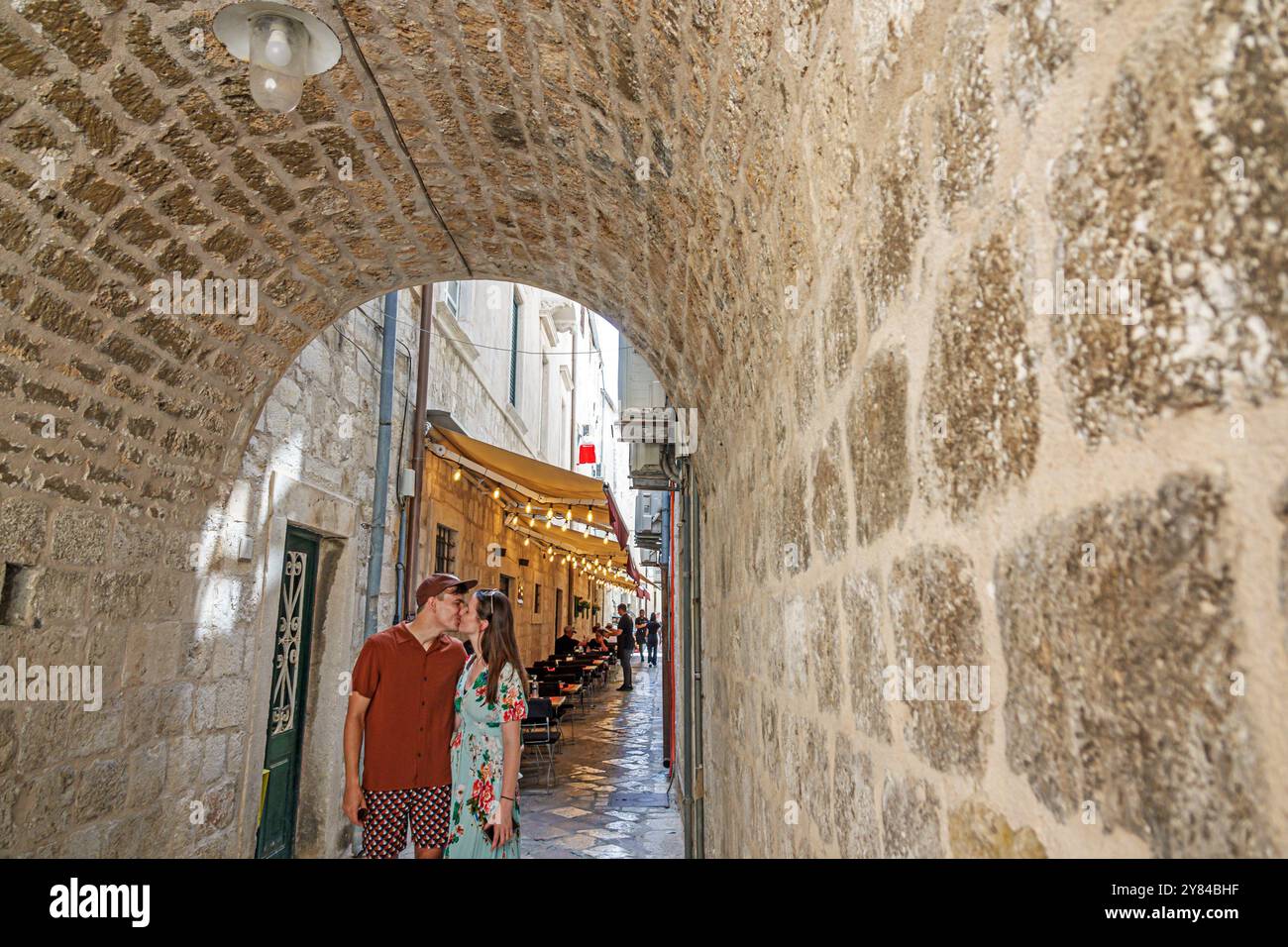 Dubrovnik Croazia, città vecchia, arco medievale delle mura della città, coppia di visitatori che baciano momento romantico, all'interno del tunnel interno, pietra calcarea pavimentata stretta pe Foto Stock