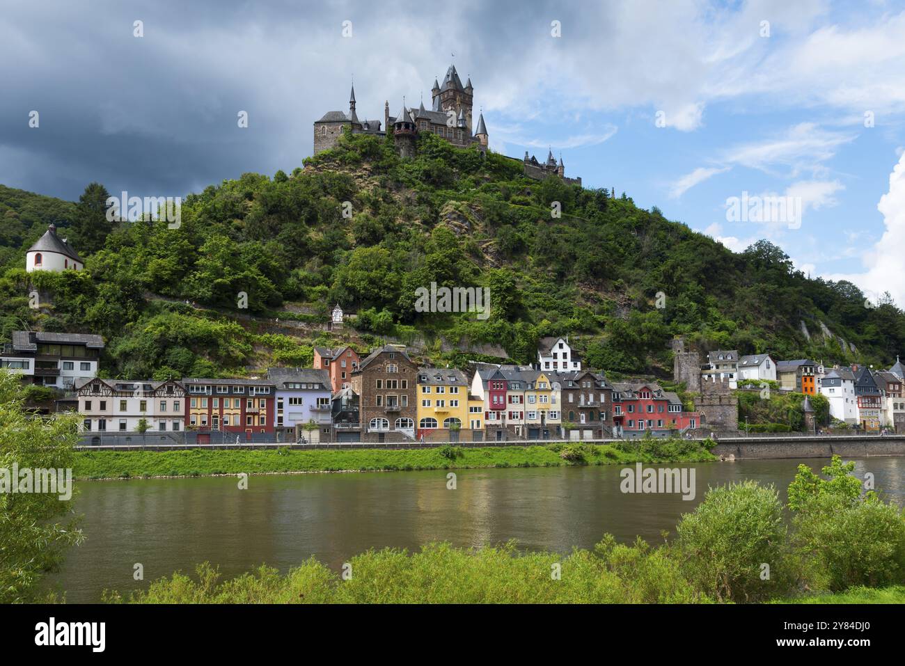 Immagine di un castello su una collina verde con edifici storici colorati lungo un fiume, cielo nuvoloso, Reichsburg, Cochem, Cochem-Zell, Mosella, Renania-Pa Foto Stock