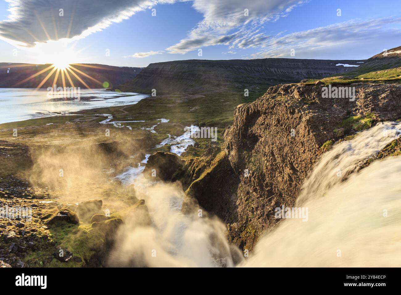 Cascata, sole di mezzanotte, stella del sole, nuvole, montagne, costa, Dynjandi, Westfjords, Islanda, Europa Foto Stock