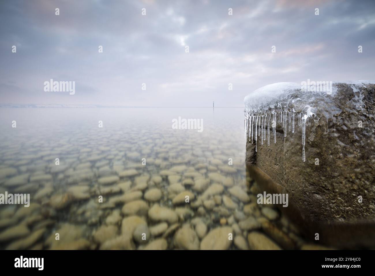 Grande masso con ghiaccioli sulla riva di un lago limpido sotto un cielo nuvoloso in inverno, Strandbad Hoernle, Costanza, Lago di Costanza, Baden-Wuerttemberg Foto Stock