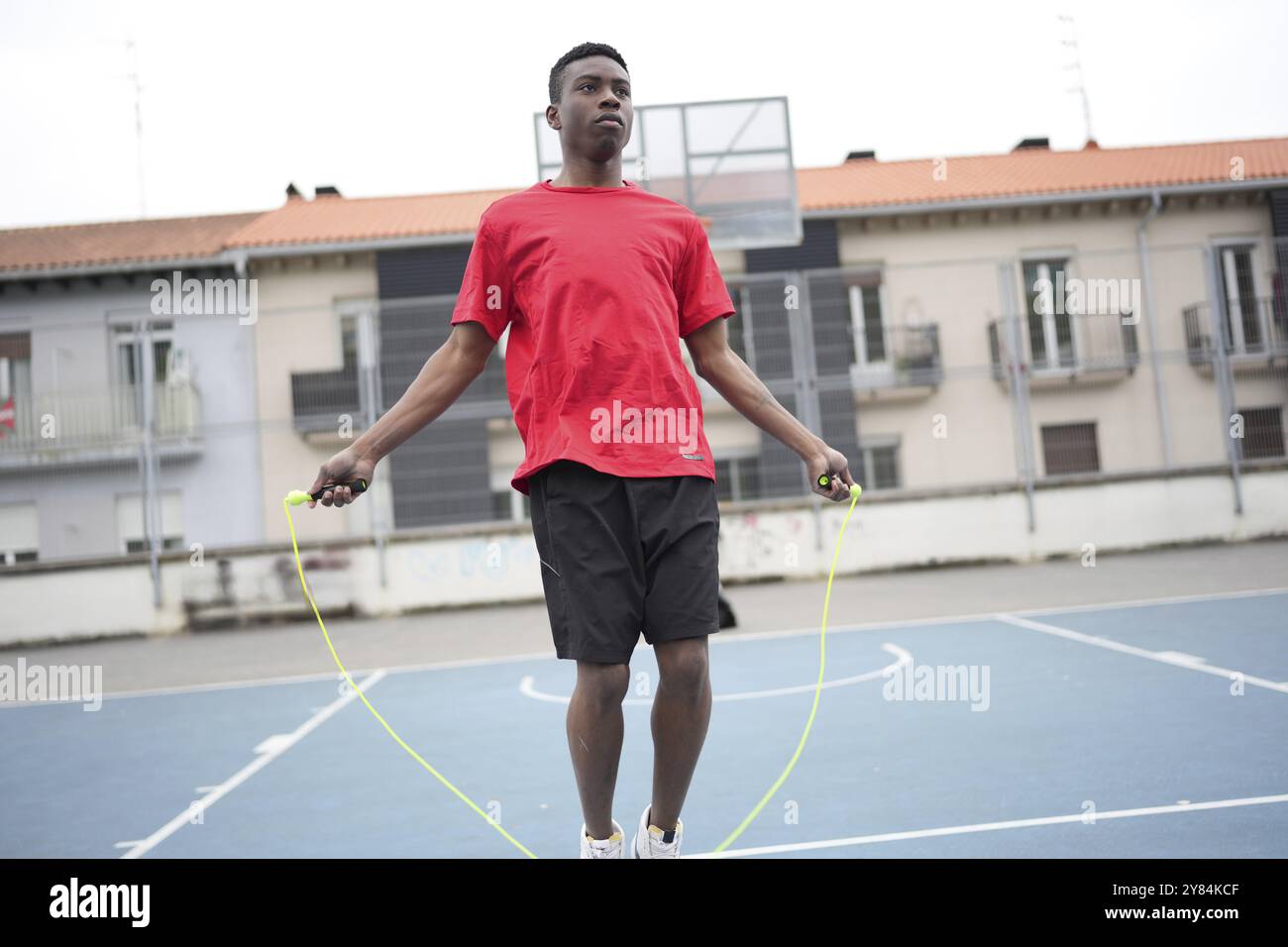 Giovane atleta africano che salta la corda per riscaldarsi in un campo da basket blu urbano Foto Stock