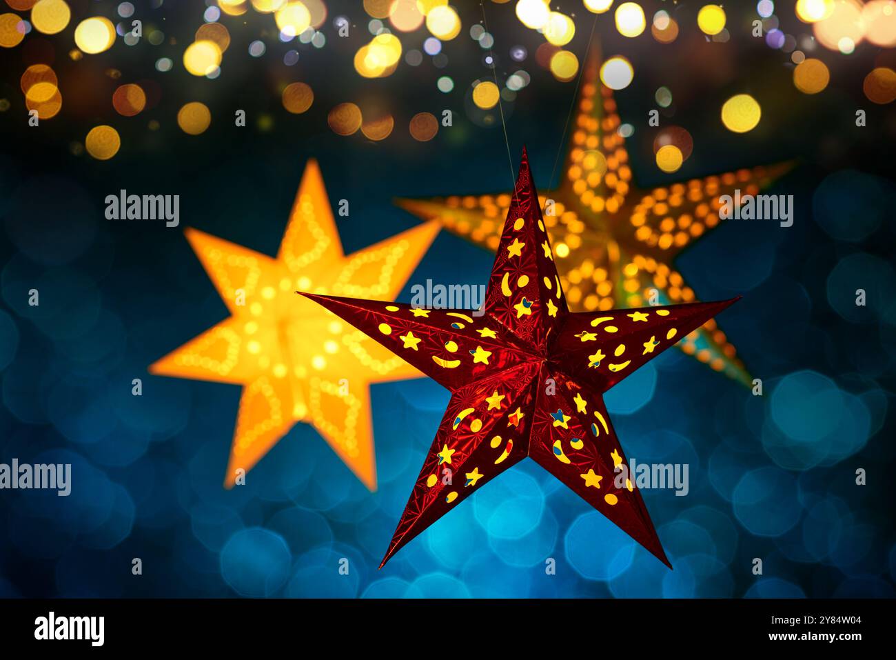 Le lanterne natalizie sono appese con luci astratte sfocate. Tre pezzi ornamentali illuminati su sfondo blu scuro con un effetto bokeh festoso Foto Stock