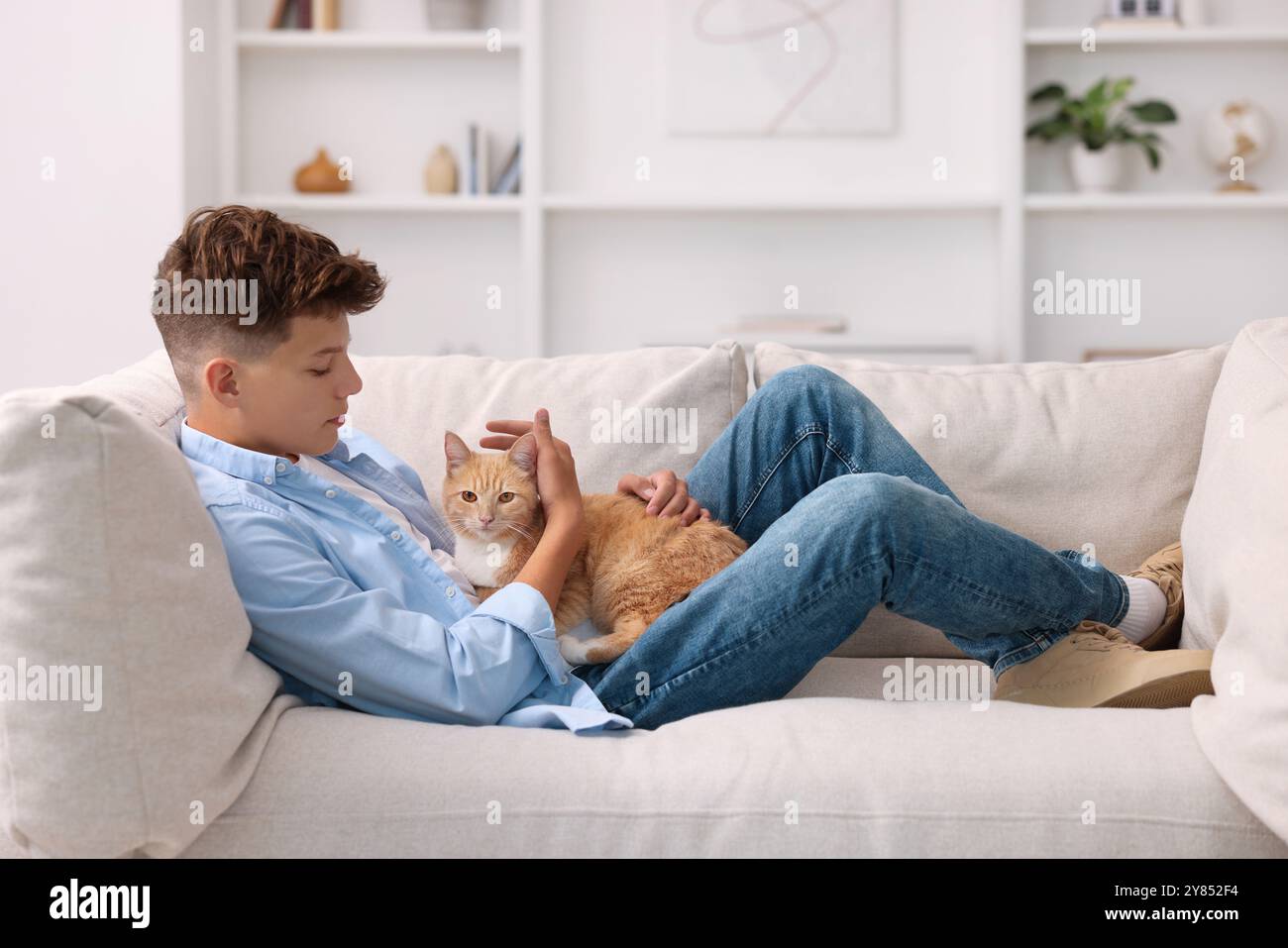 Concetto di solitudine. Triste ragazzo adolescente con un gatto carino sul divano di casa Foto Stock