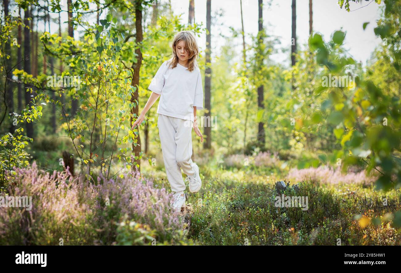 In estate un bambino si aggira con gioia attraverso una foresta verdeggiante, interagendo con le piante circostanti e godendosi la bellezza della natura. Foto Stock