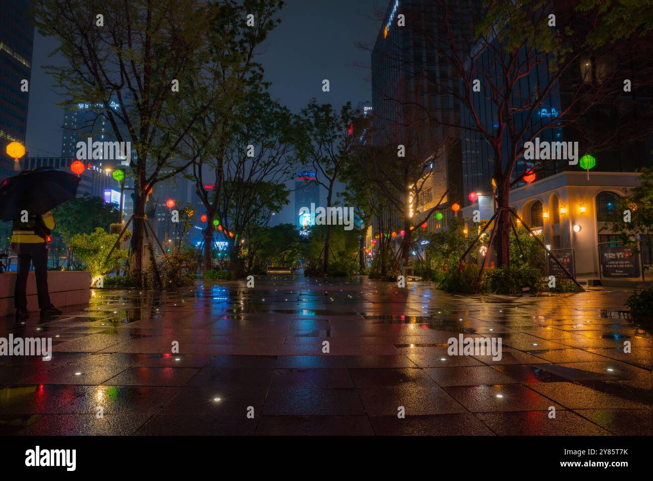 Una serata piovosa a Piazza Gwanghwamun, dove il marciapiede bagnato riflette le vivaci luci della città e le tradizionali lanterne, creando una scena serena. Foto Stock