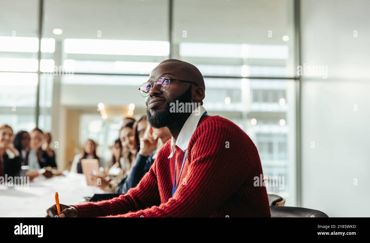 Uomo d'affari di etnia afroamericana impegnato in una conferenza di gruppo. Mette in evidenza l'interazione professionale e la partecipazione attenta, mostrando Foto Stock