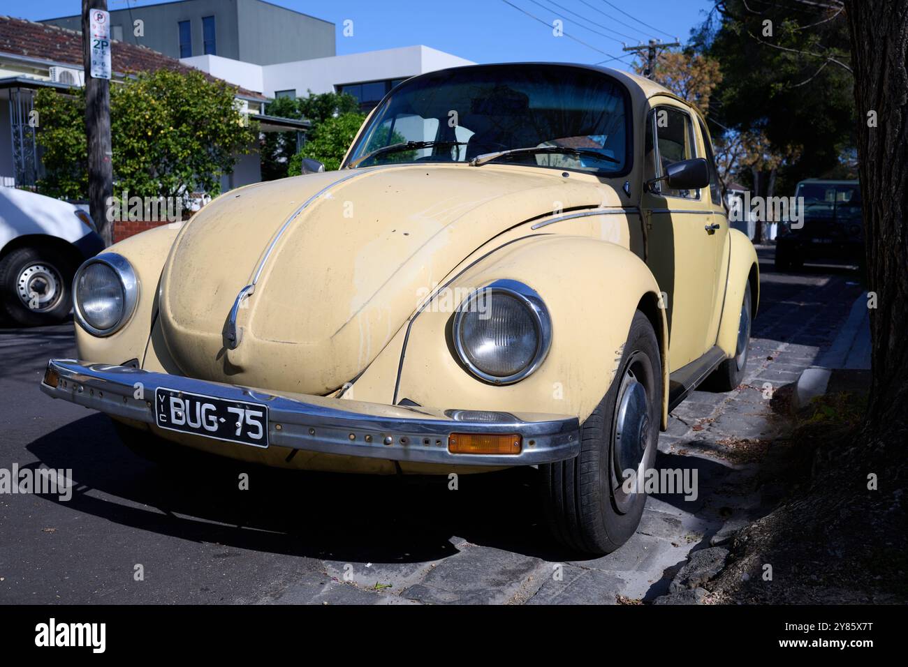Davanti a un vecchio Maggiolino Volkswagen giallo o crema, con targa personalizzata che fa riferimento al soprannome VW bug, parcheggiato sulla strada Foto Stock