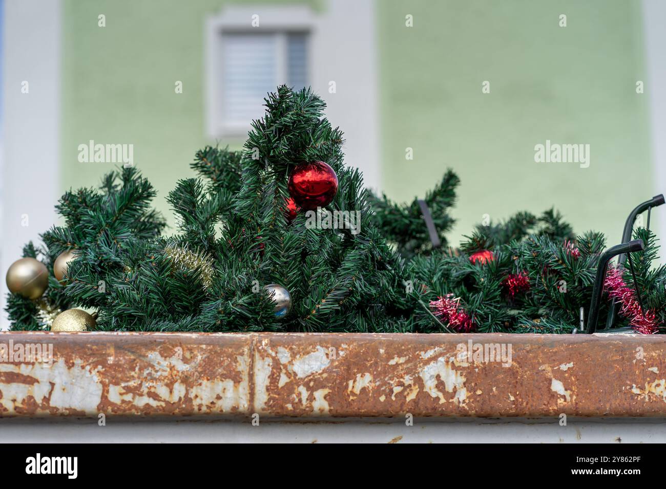 Abeti di plastica smaltiti decorati con palle di Natale rosse in un contenitore della spazzatura. Foto Stock