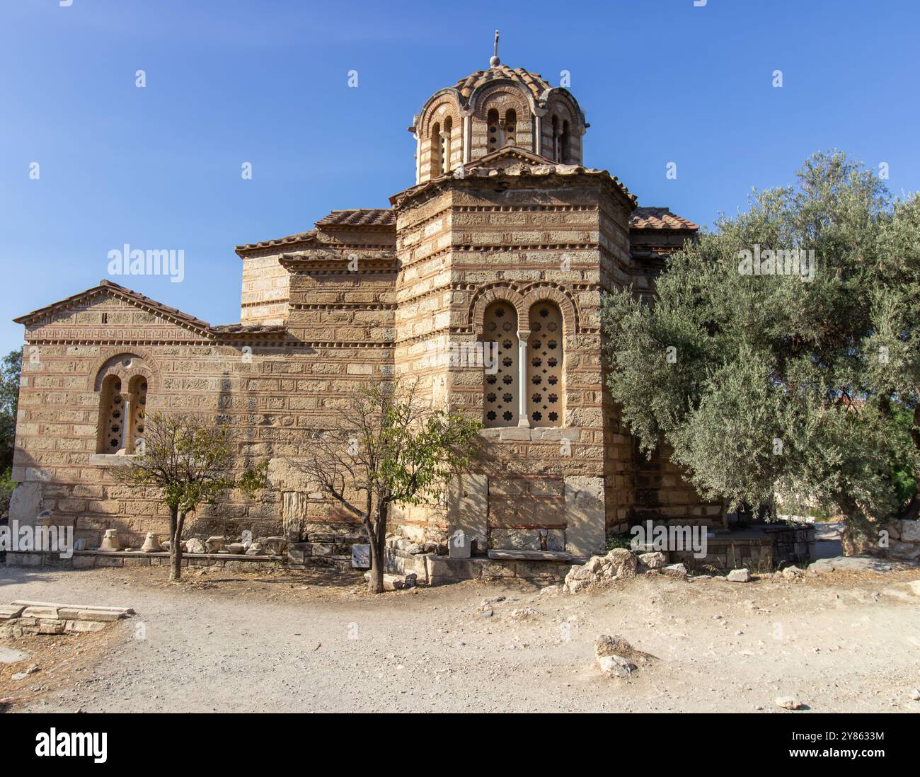 Antica chiesa in pietra in stile bizantino con tetto a cupola e croce sulla sommità, circondata da alberi e sentieri ad Atene, Grecia. Fotograp architettonico all'aperto Foto Stock