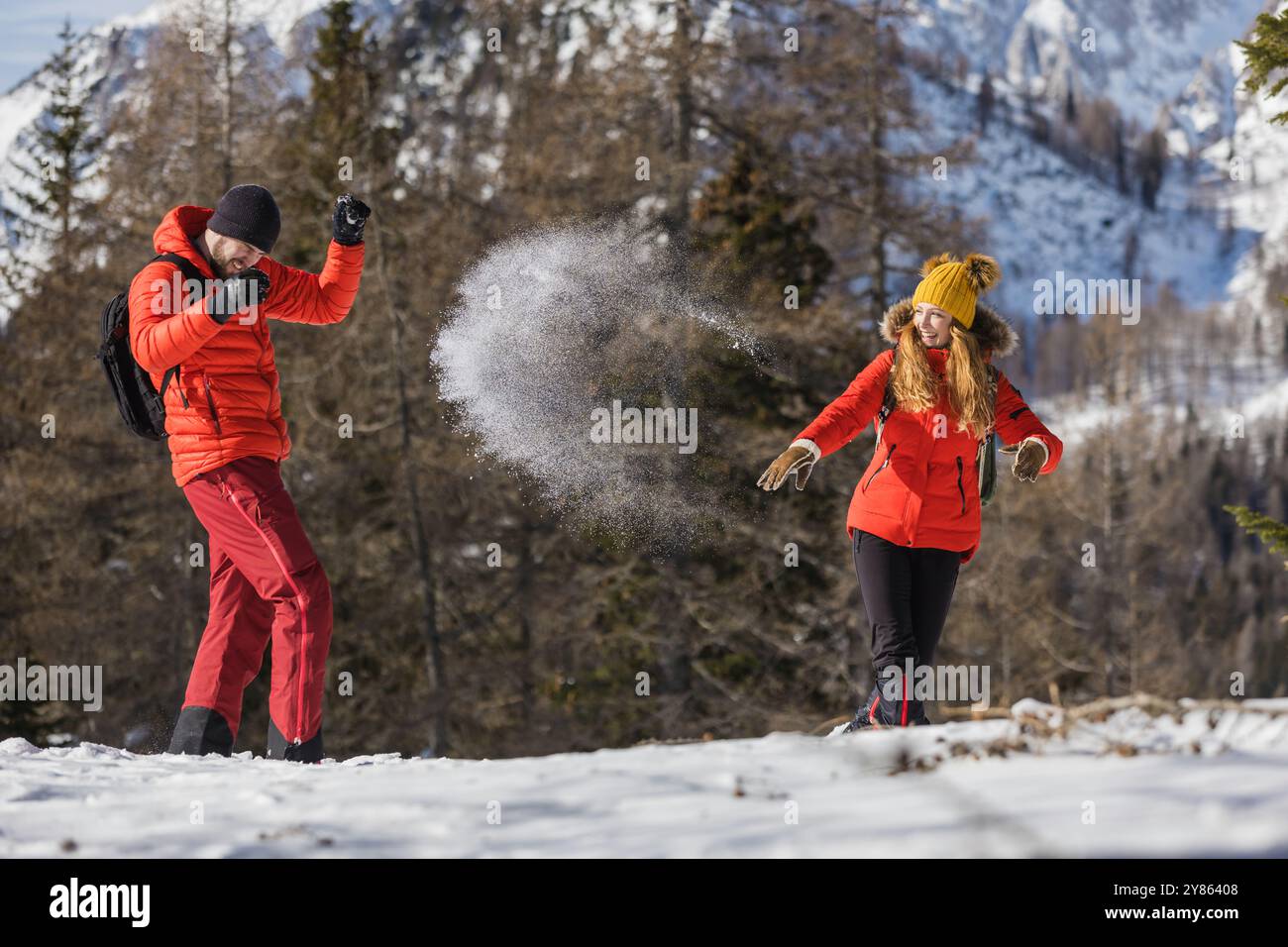 La coppia gioca a gettare la neve in una giornata di sole all'aperto tra le montagne innevate Foto Stock
