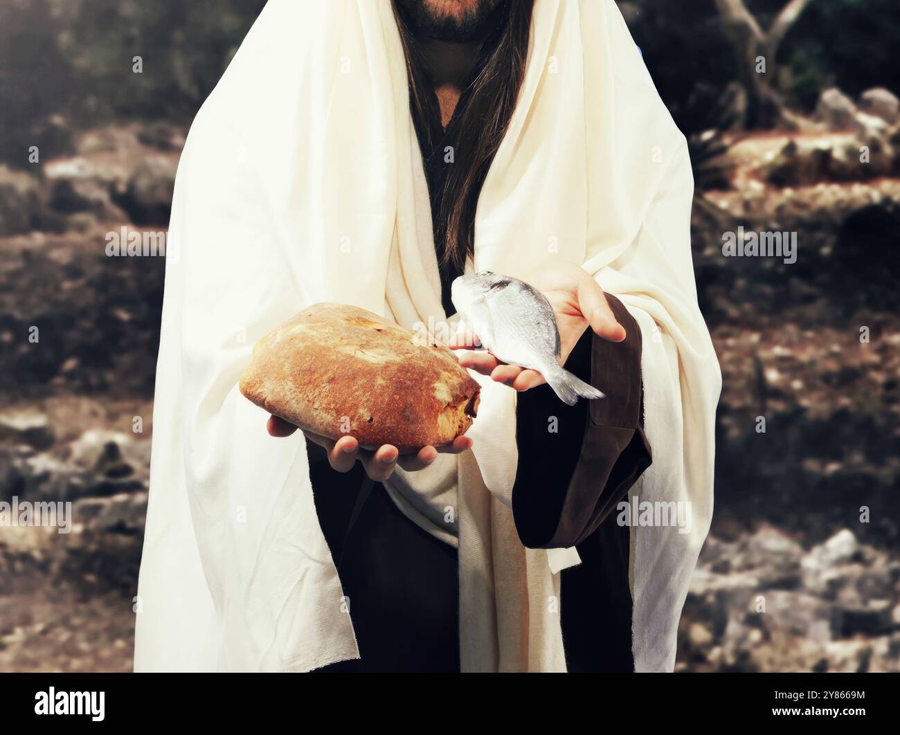 Gesù cristo indossa una veste biblica, sta in piedi all'aperto e tiene in mano una pagnotta di pane e un pesce Foto Stock