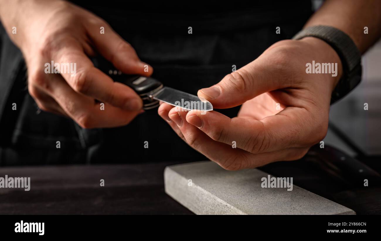 Mani da uomo con coltello pieghevole e strumento per affilare la pietra. coltello per affilatura principale su una mola Foto Stock