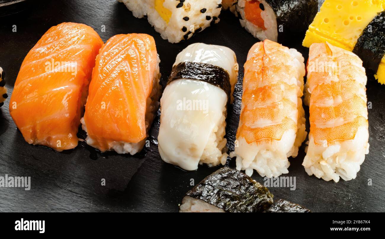 Primo piano di molti tipi diversi di sushi nigiri seduti su una superficie di ardesia nera Foto Stock