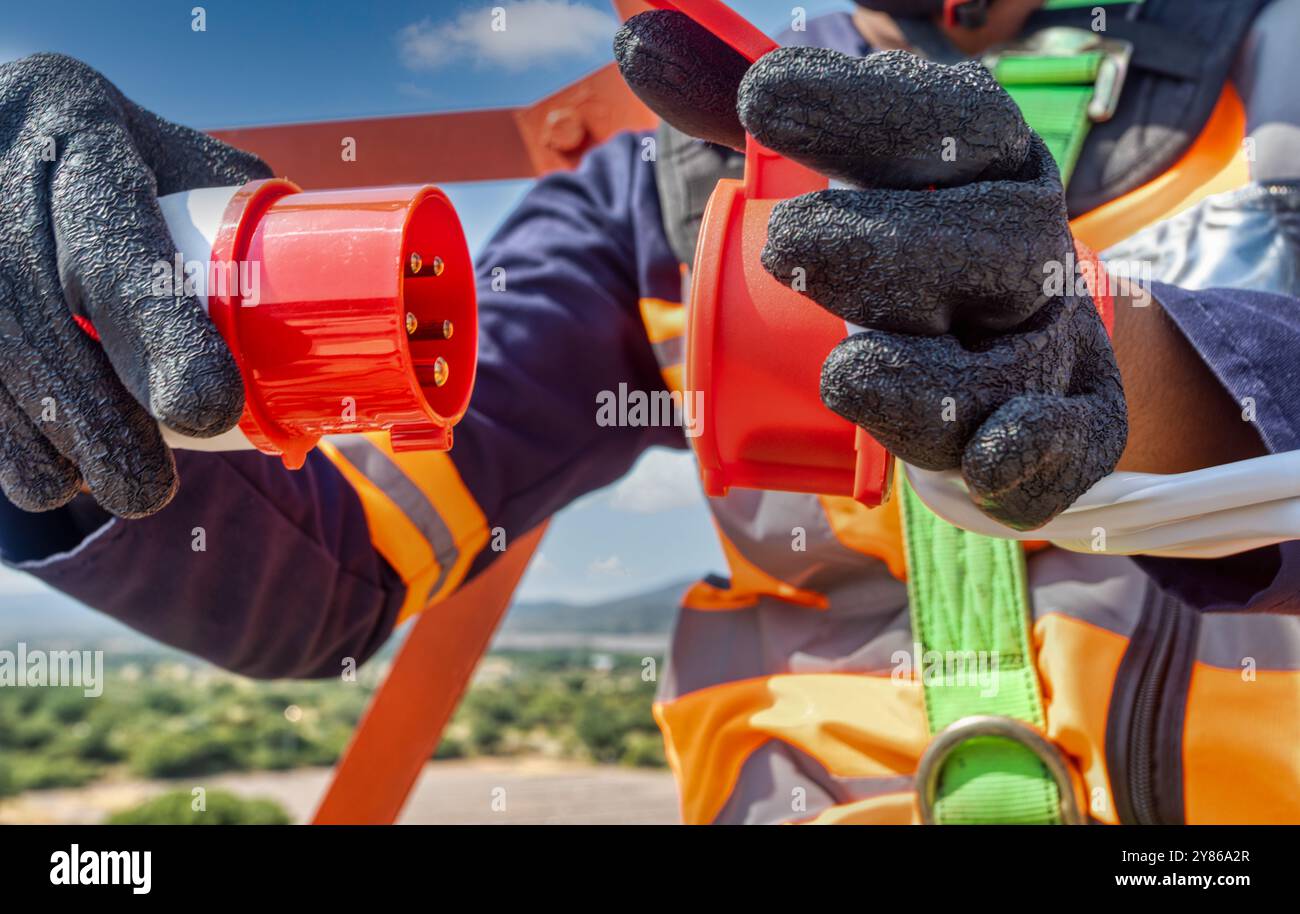 Vista aerea elettricista in alto sulla torre, presa ad alta tensione in mano. Collegamento di una presa trifase ad alta tensione da 380 V, costo dell'elettricità, elettrico Foto Stock