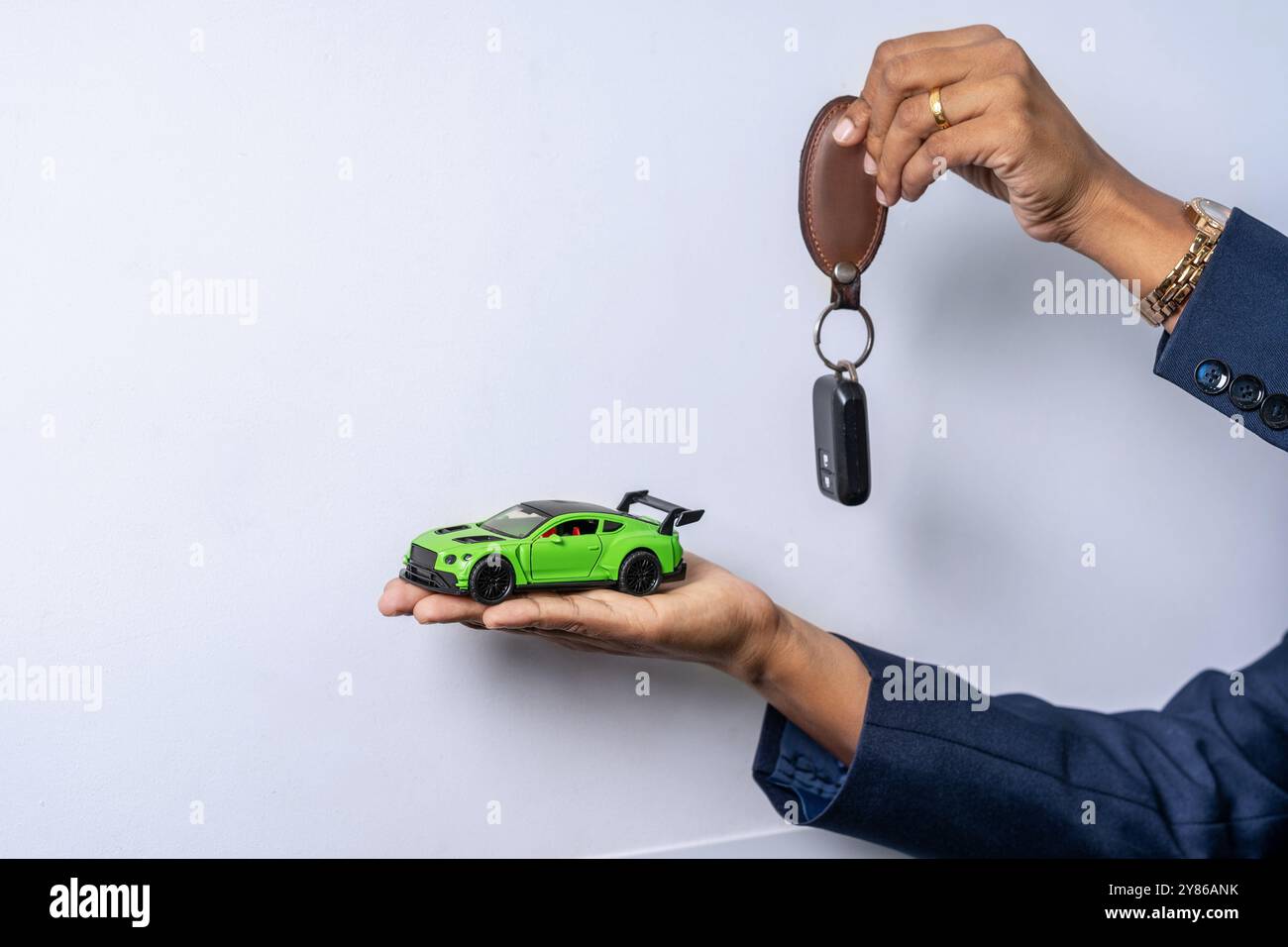 Un primo piano di una donna indossa un costume che tiene in mano la chiave di un'auto e un'auto giocattolo verde su uno sfondo semplice con ampio spazio per le copie simboleggia la proprietà dell'auto Foto Stock
