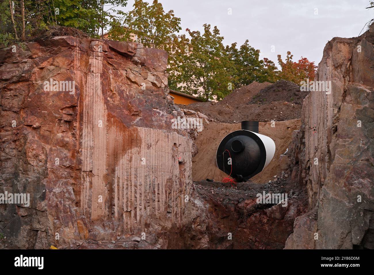 Questa immagine mostra un sito di scavo in cui viene installato un grande serbatoio industriale, possibilmente un serbatoio di acqua o fognatura. Il sito è circondato da rocce Foto Stock
