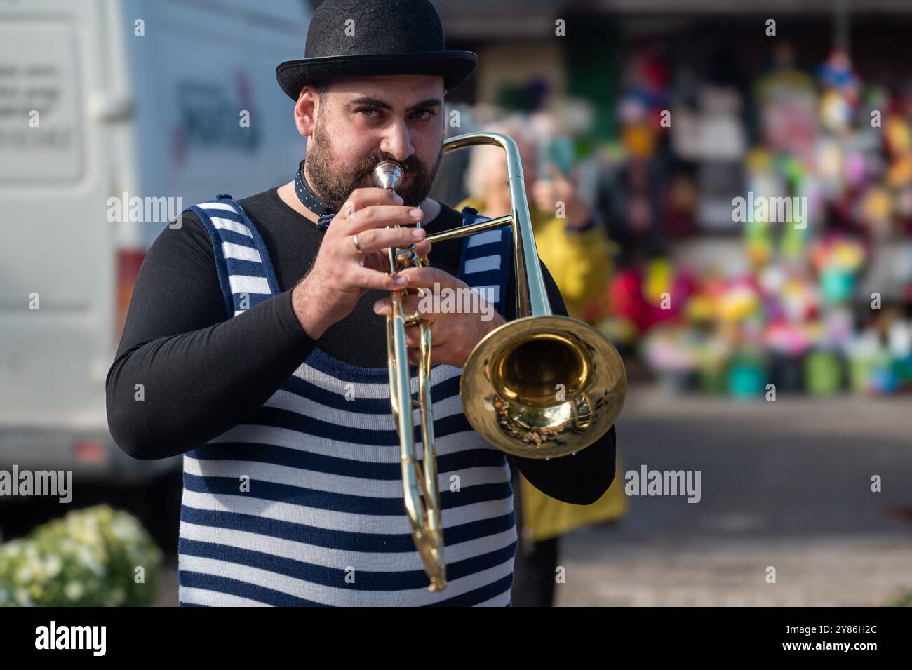 Tukums, Lettonia - 28 agosto 2024: Un musicista vestito di strisce si esibisce con una tromba in un vivace mercato all'aperto. Foto Stock