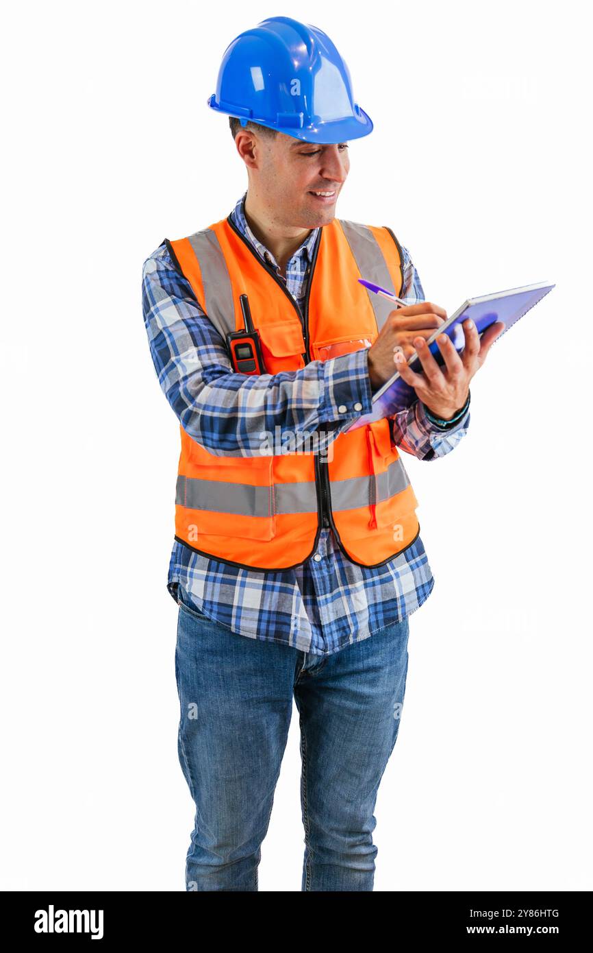 l'operaio edile verticale, vestito con un giubbotto di sicurezza arancione e un elmetto, scrive su un notebook con una penna, sfondo bianco. L'immagine viene evidenziata Foto Stock