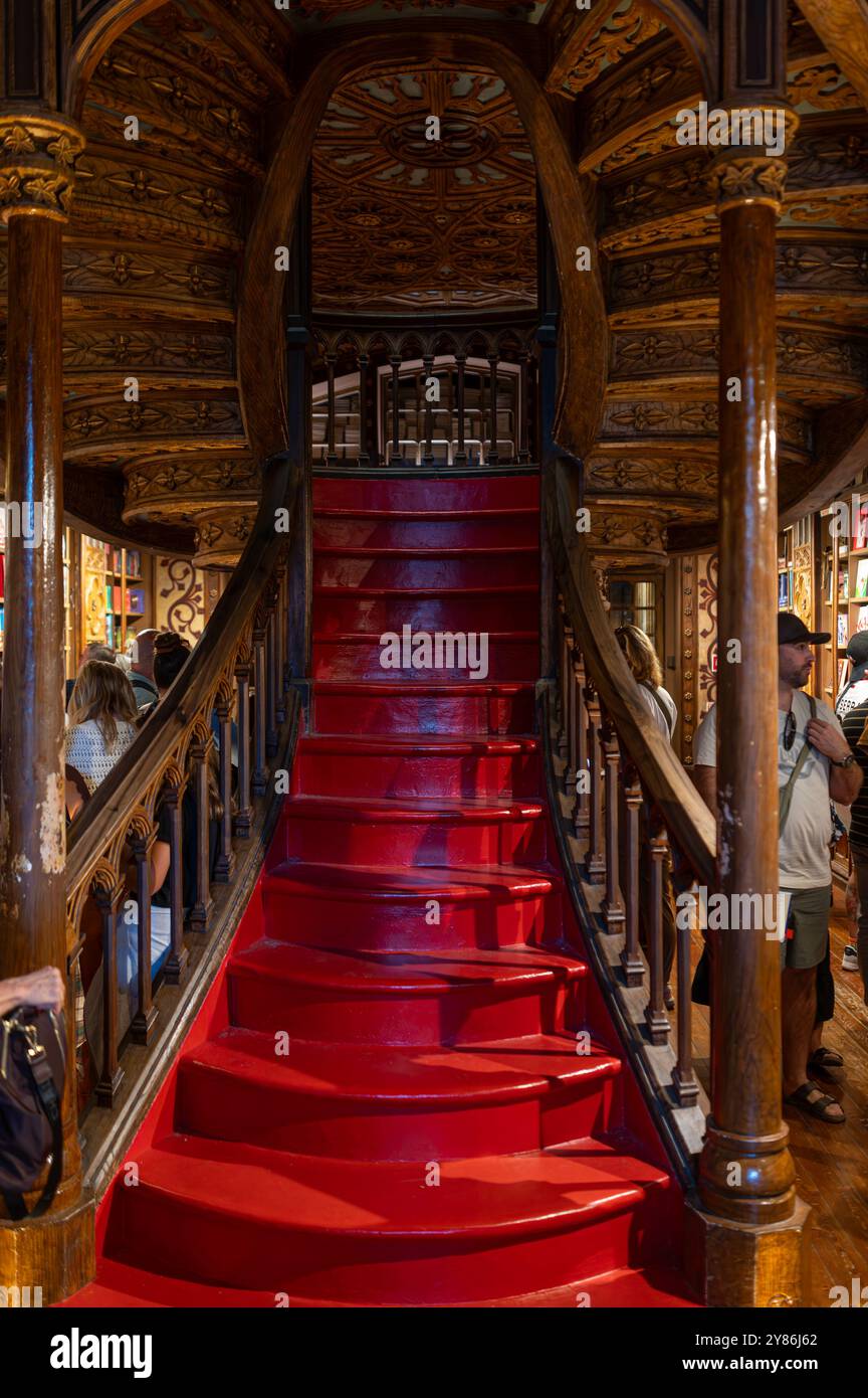 Porto, Portogallo - 12 settembre 2024 : i visitatori esplorano un'affascinante libreria con una scalinata rossa ornata e mensole in legno Foto Stock