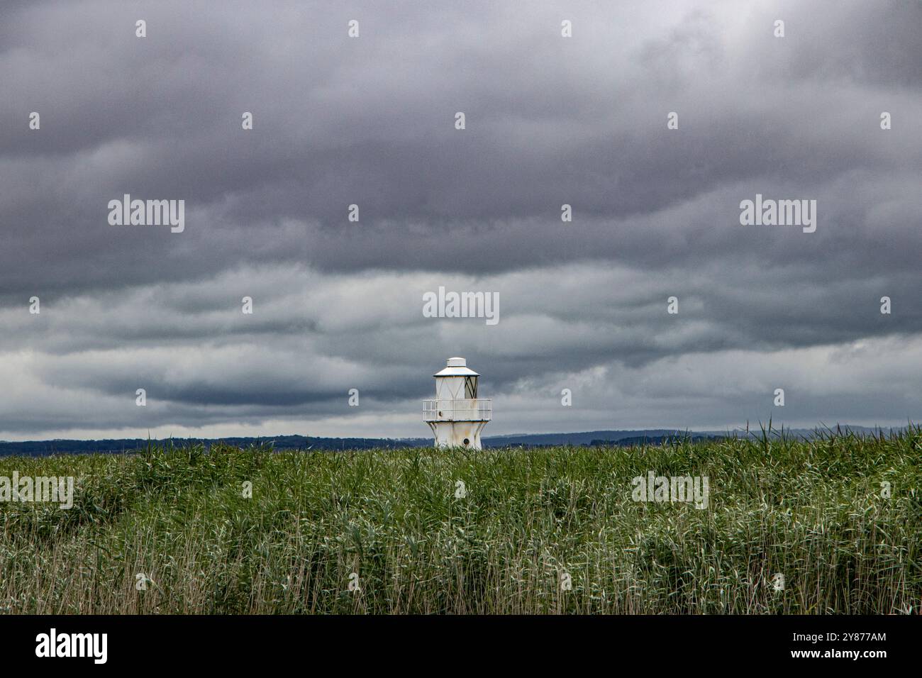Faro di Usk Est dietro un campo di verde e contro un cielo grigio scuro Foto Stock
