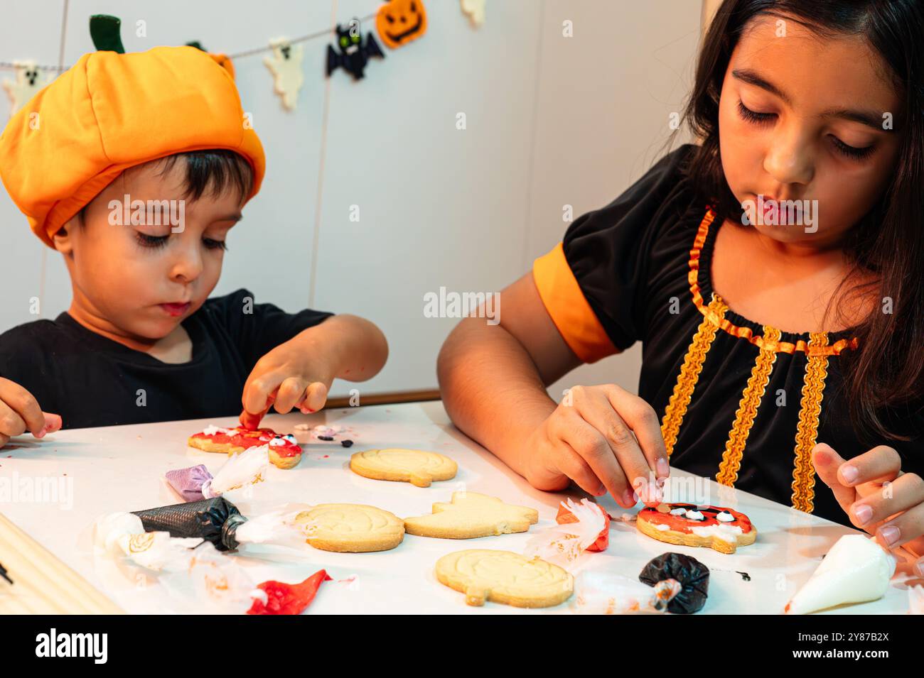 Una ragazza e un ragazzo stanno facendo i biscotti di Halloween. La ragazza indossa un vestito nero e il ragazzo indossa una camicia nera Foto Stock