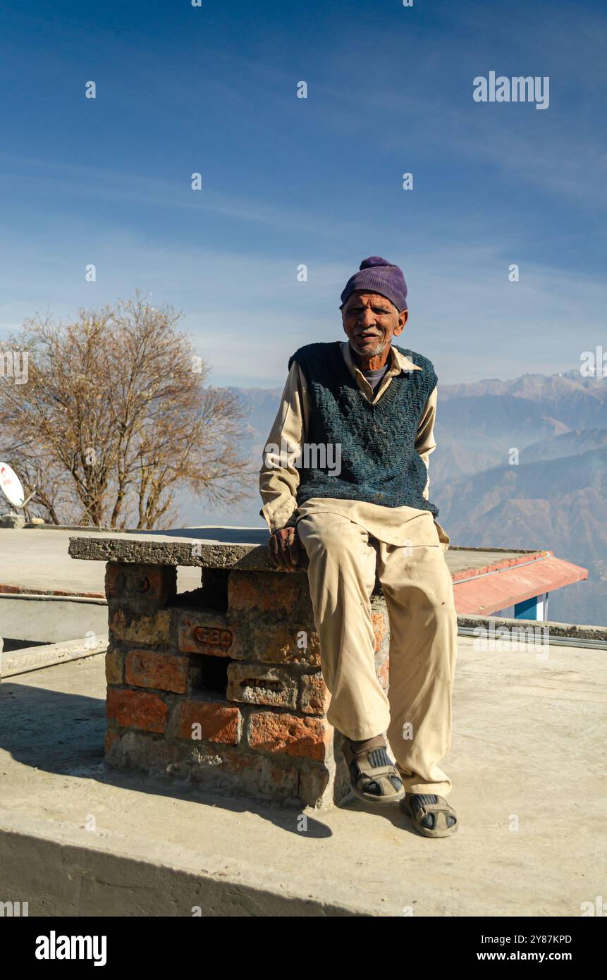 Una persona anziana seduta in cima a un camino in un villaggio in Himachal Pradesh, India Foto Stock