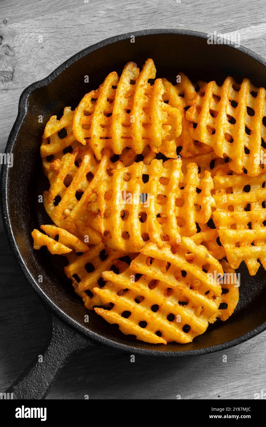 Le patatine fritte sono preparate in una padella in ghisa su un tagliere di legno. Concetto di fast food malsano Foto Stock