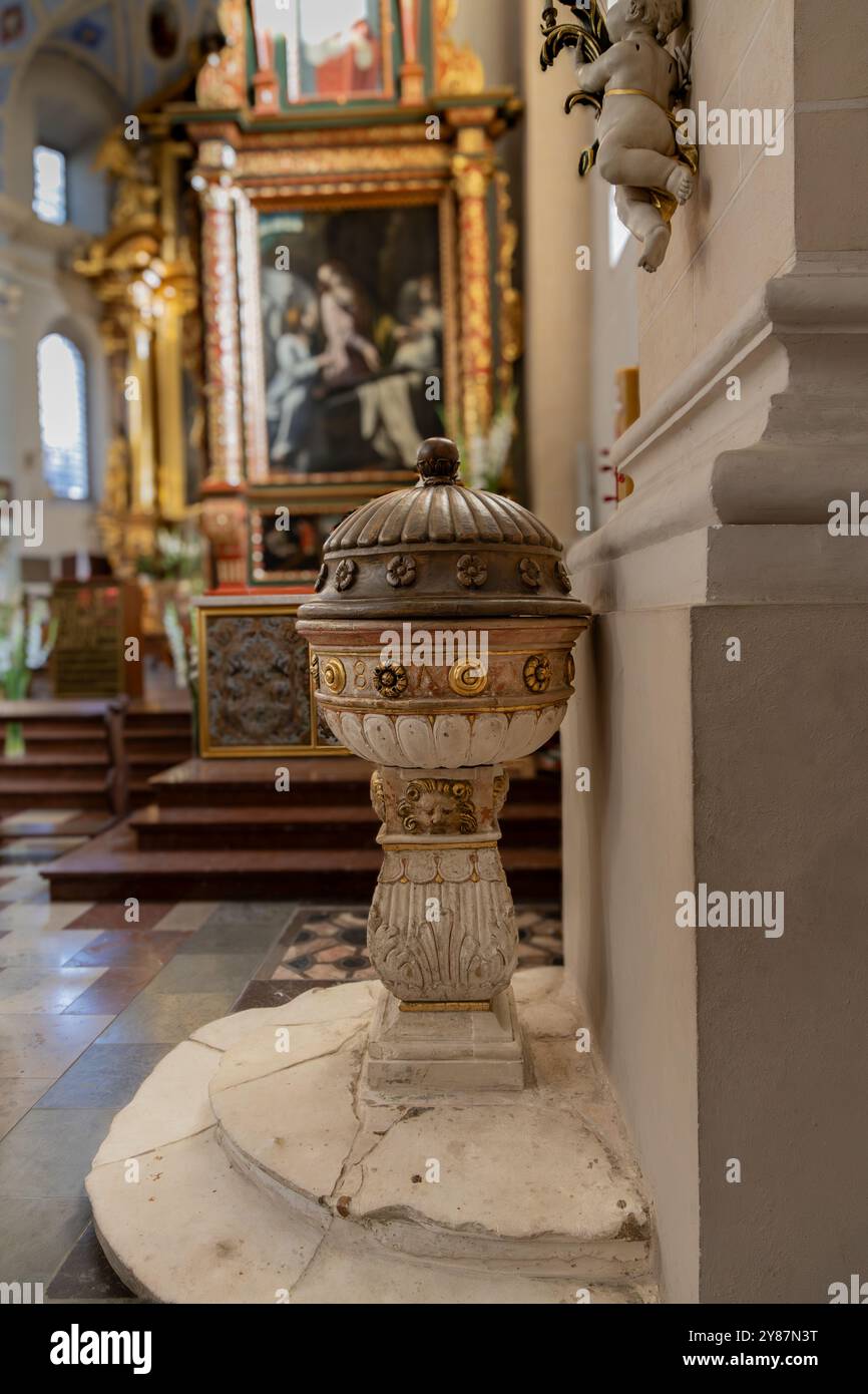 Cattura la serena bellezza dell'arte religiosa con questa splendida fotografia con un elegante fonte battesimale adagiata contro l'interno storico di un WE Foto Stock